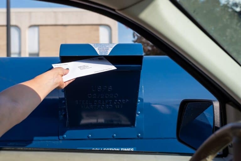 A woman is mailing an envelope in a drive thru mail box at a US Post Office - vote by mail concept