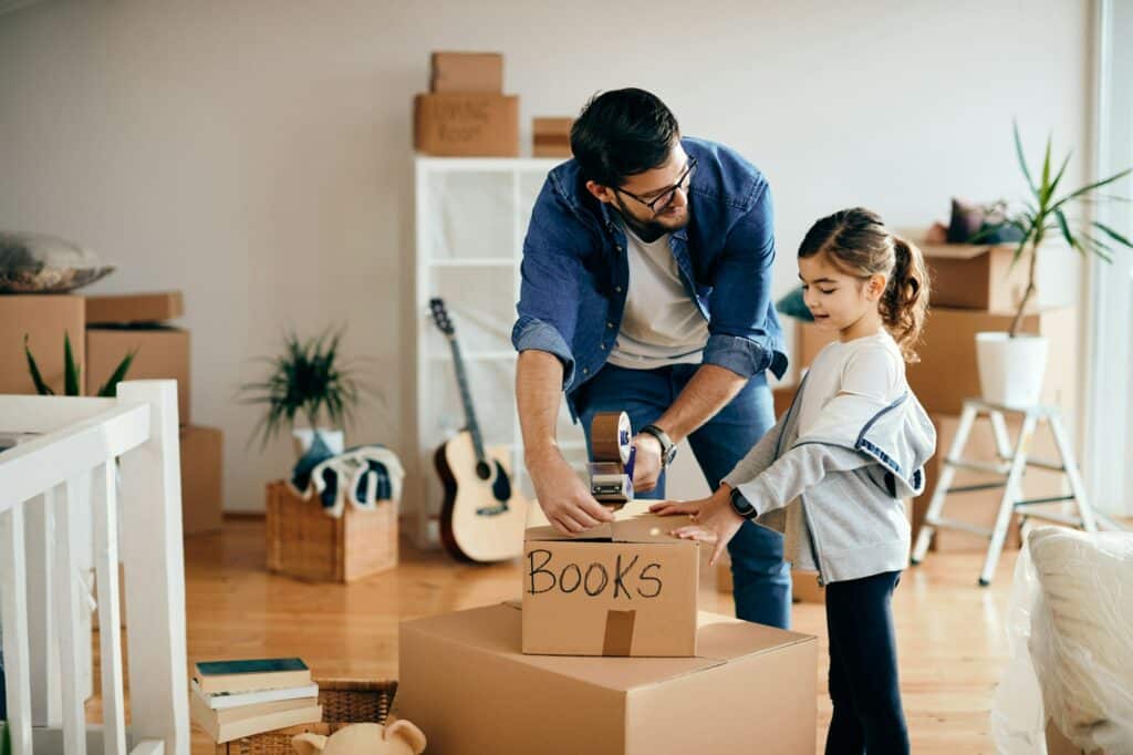 Happy little girl and her father packing cardboard boxes while relocating into a new home.