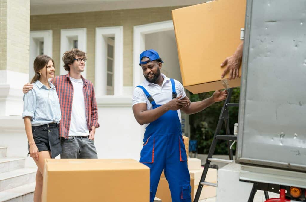 Man movers worker in blue uniform unloading cardboard boxes from truck for moving house service