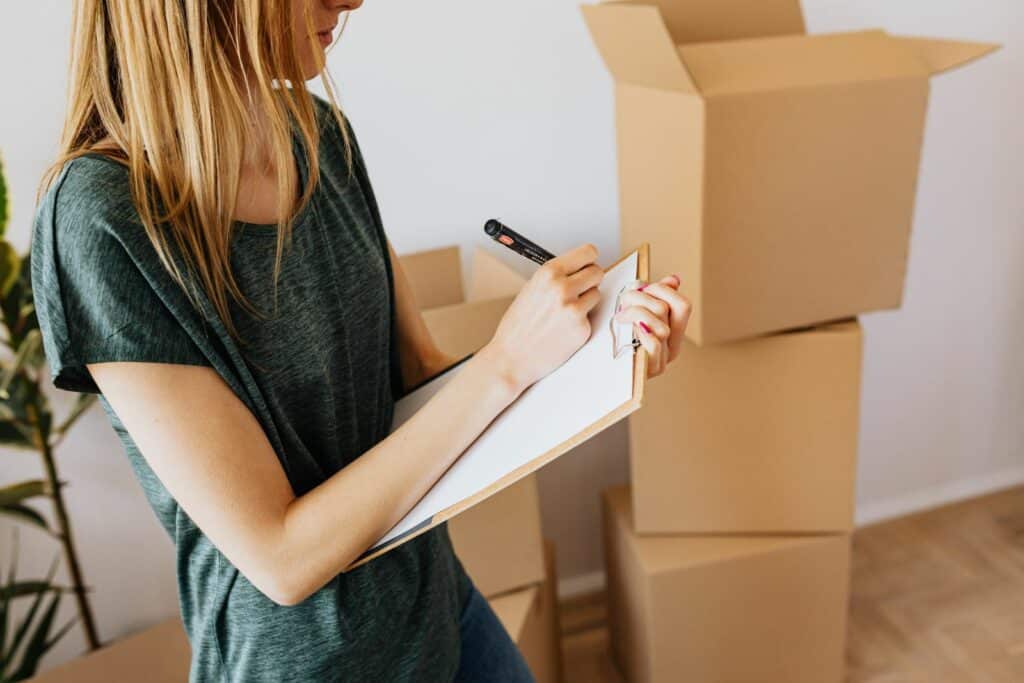 Person taking notes beside packed moving boxes while preparing building paperwork for a move
